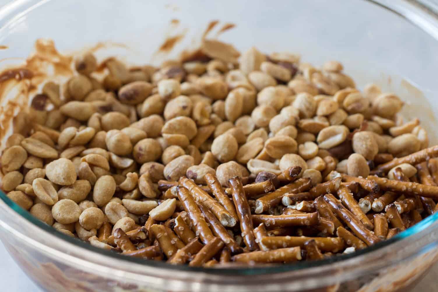 Glass bowl filled with peanuts and pretzel sticks on top of a melted chocolate peanut butter mixture.