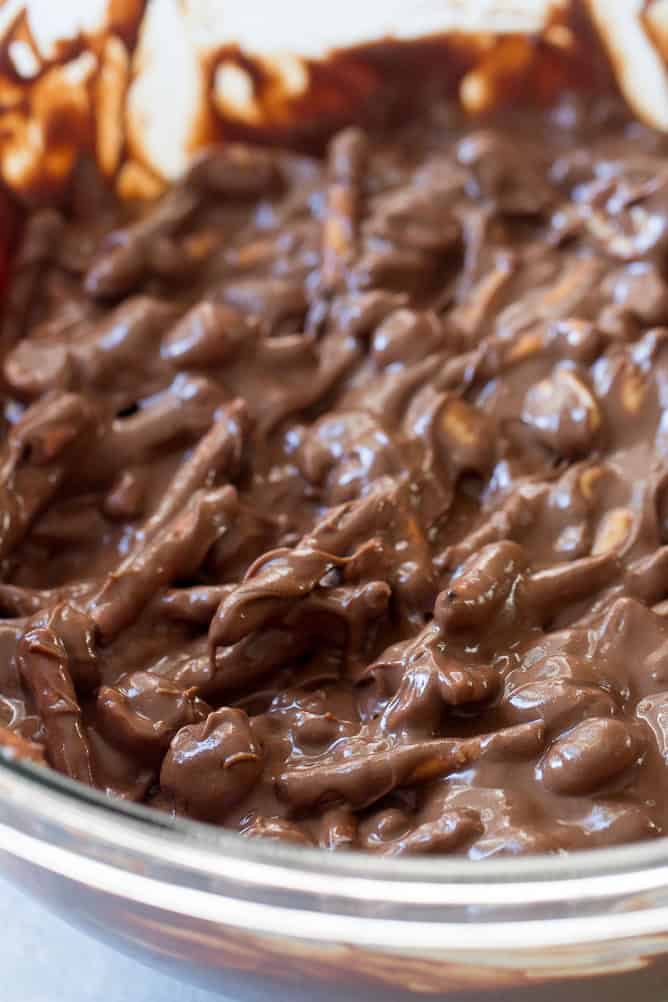 Pretzel sticks and peanuts mixed into chocolate peanut butter sauce in a glass bowl.