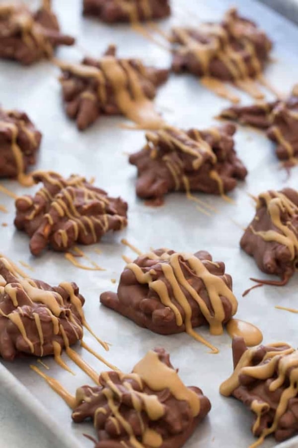 A baking sheet with clusters of chocolate-covered pretzels, drizzled with peanut butter, is arranged in rows.