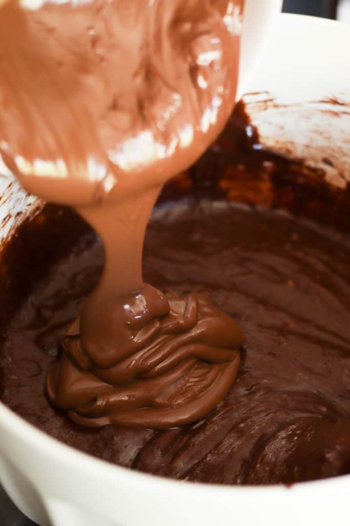 Pouring melted nutella on top of unbaked brownie layer in baking dish.