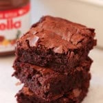 Three chocolate brownies stacked in front of a jar labeled "Nutella.
