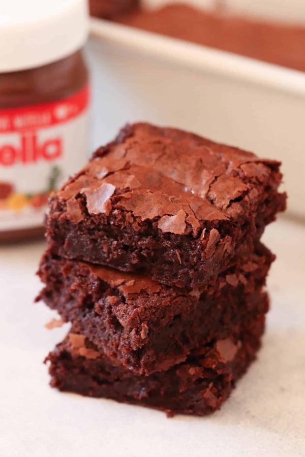 Three chocolate brownies stacked in front of a jar labeled "Nutella.