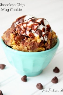 Chocolate Chip Mug Cookie in a mug with whip cream and chocolate sauce. Chocolate chips surrounding the mug.
