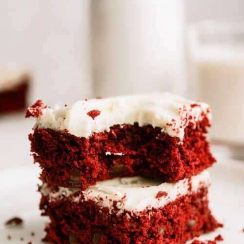 Red Velvet Brownies with White Chocolate Buttercream Frosting stacked on a plate with a bite missing out of the top brownie.