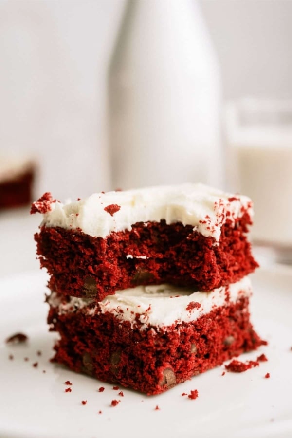 Red Velvet Brownies with White Chocolate Buttercream Frosting stacked on a plate with a bite missing out of the top brownie.