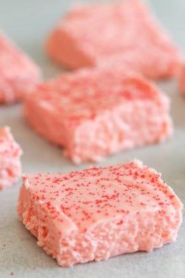 Close-up of pink marshmallow squares with red sprinkles on top, arranged on a light-colored surface.
