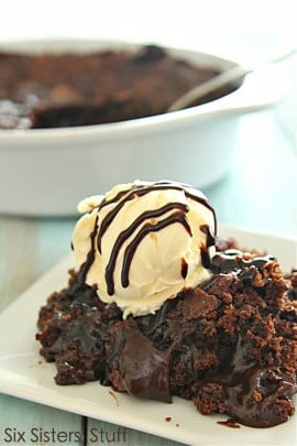 A close-up of a chocolate dessert served on a white plate, topped with a scoop of vanilla ice cream drizzled with chocolate sauce.