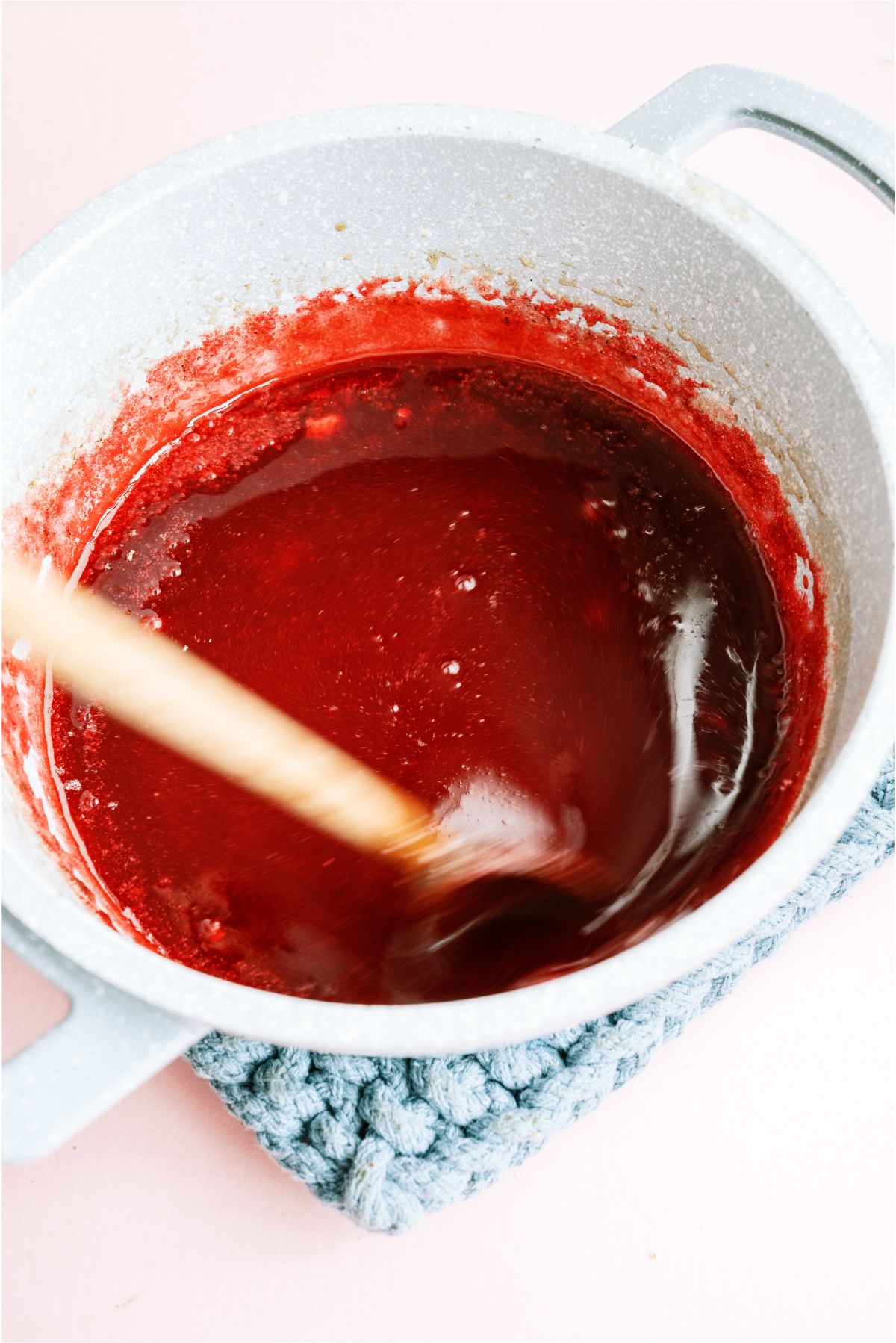 Strawberry sauce ingredients in saucepan with with wooden spoon