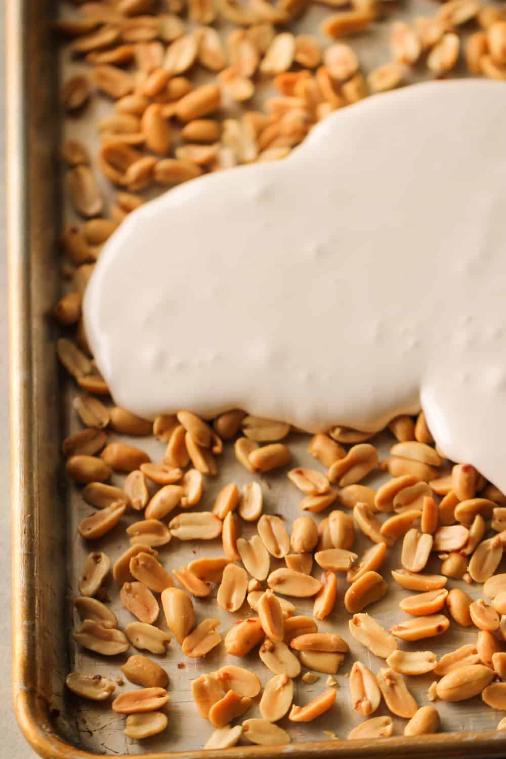 Peanut on the bottom of a cookie sheet with the marshmallow mixture being poured on top.