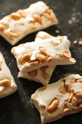 Close-up of nougat candy pieces containing peanuts, displayed on a dark surface.