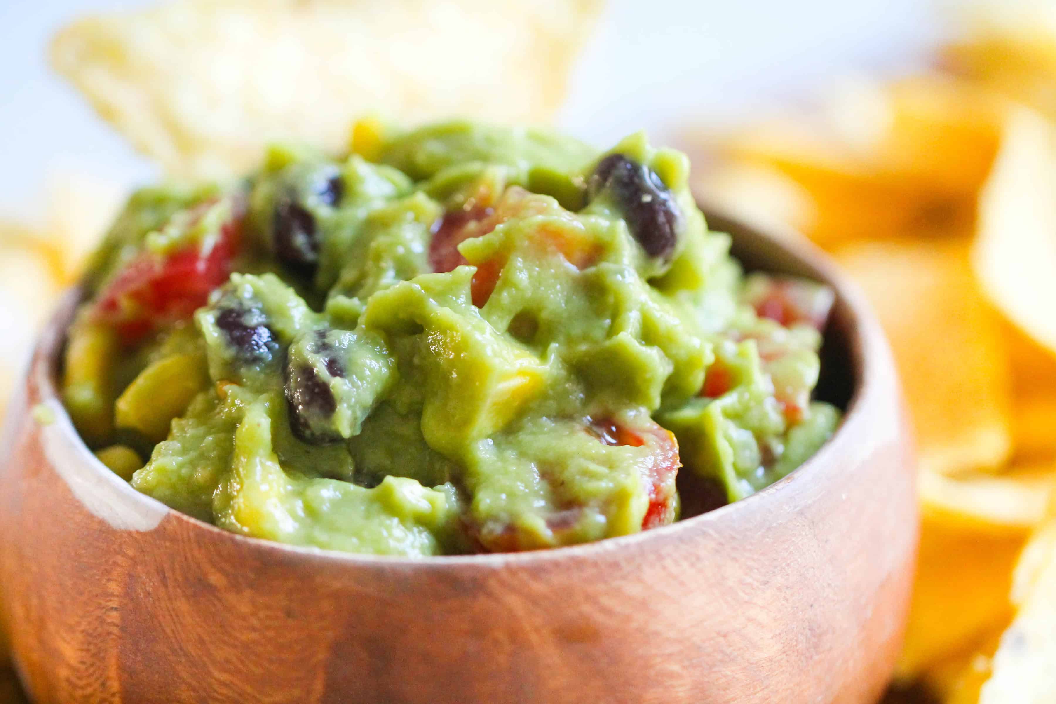 A scoop of guacamole, containing chunks of tomato, beans and corn.