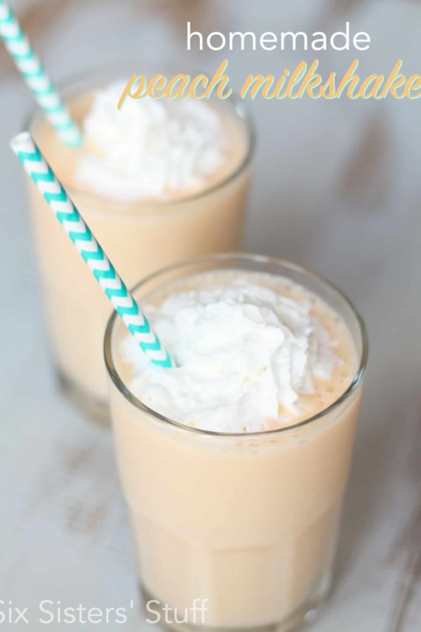 Two glasses of peach milkshake topped with whipped cream and served with green and white striped straws.