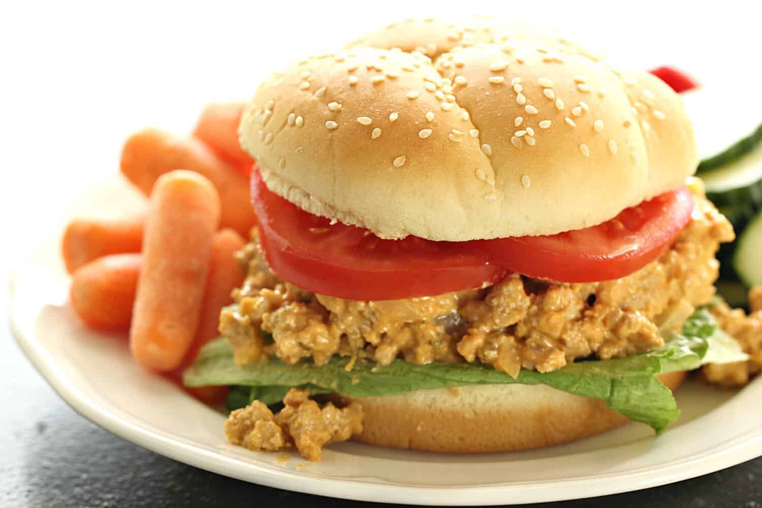 Slow Cooker Cheesy Turkey Burger Joes on a bun plated with vegetables