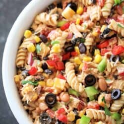 A bowl of pasta salad with rotini, black olives, corn, bell peppers, beans, and a creamy dressing.