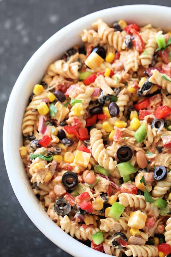 A bowl of pasta salad with rotini, black olives, corn, bell peppers, beans, and a creamy dressing.