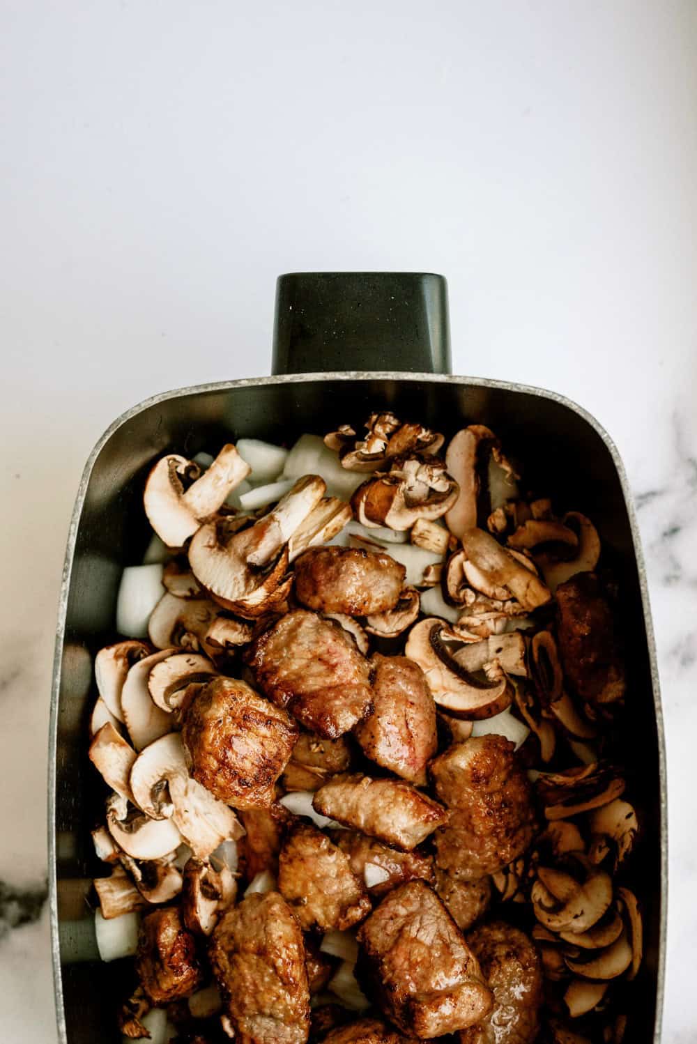 Onions and mushrooms mixed with beef tips in the slow cooker