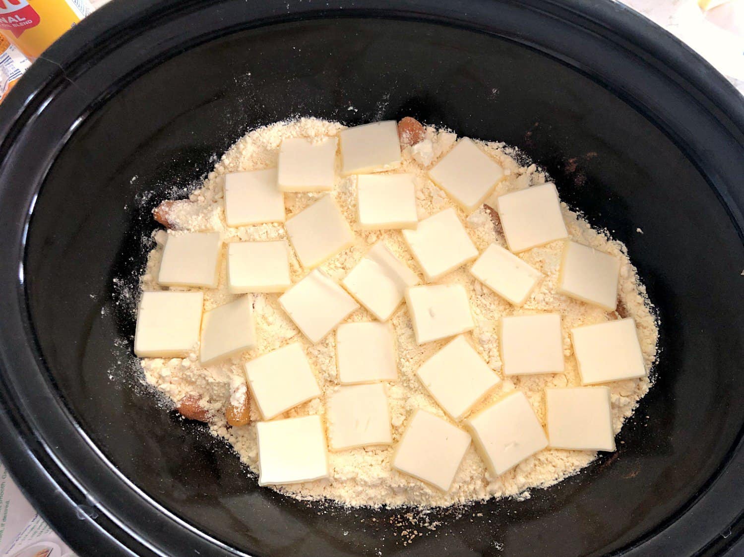 Unbaked Peach Cobbler in the crock pot topped with butter slices