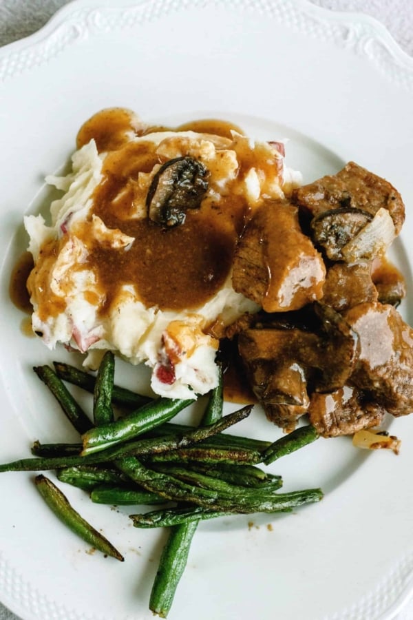 Plate with mashed potatoes topped with gravy, sirloin tips, and green beans on the side.
