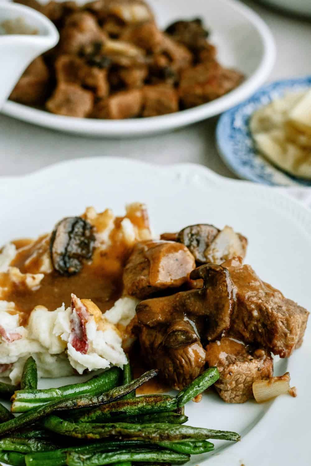 Slow Cooker Beef Sirloin Tips and Gravy on a white plate served with green beans and mashed potatoes