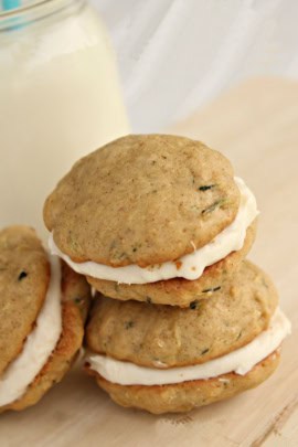 Close-up of three zucchini whoopie pies with cream filling stacked on a light-colored surface with a blurred milk bottle in the background.