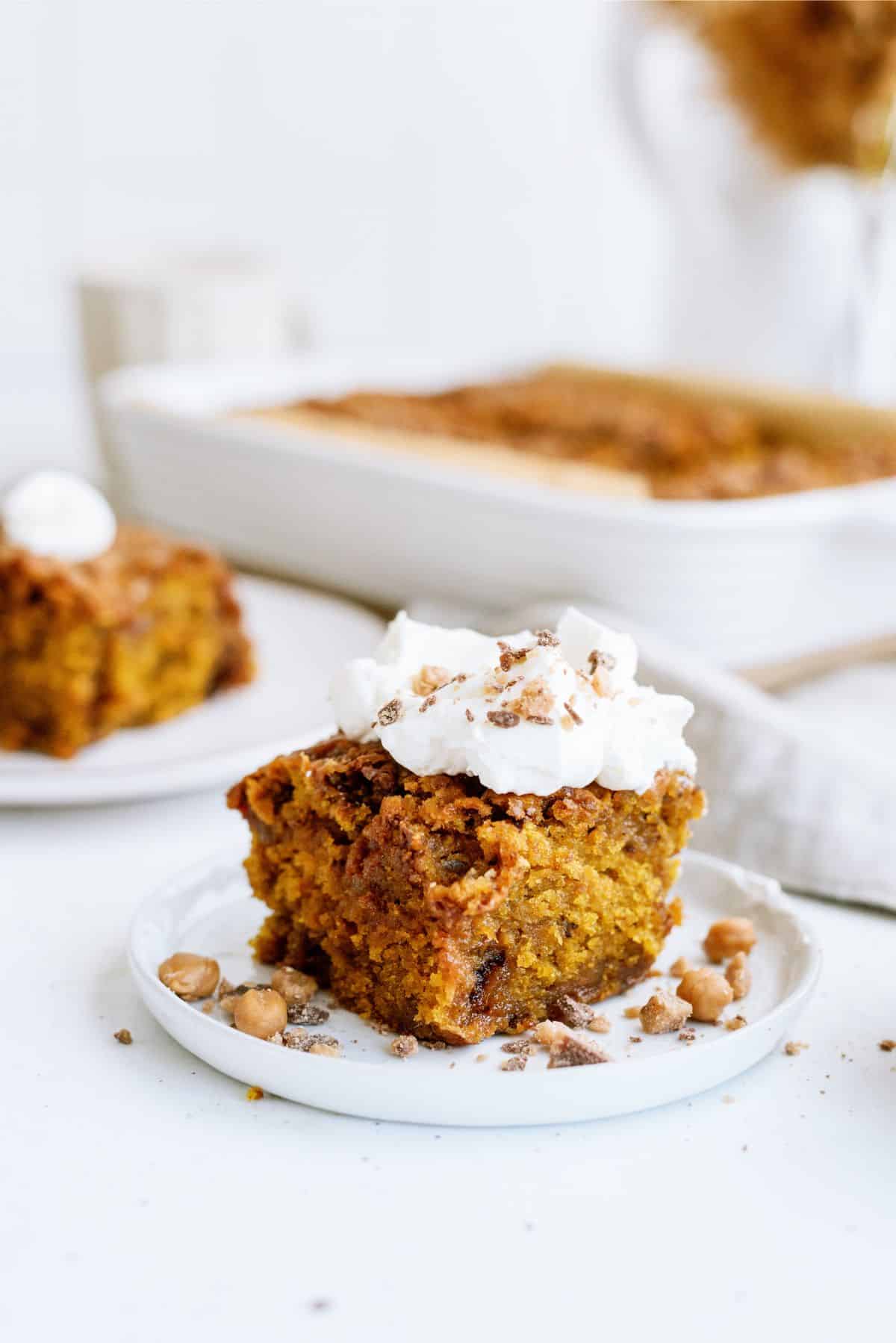 Slice of Caramel Toffee Pumpkin Cake on a plate topped with whip cream