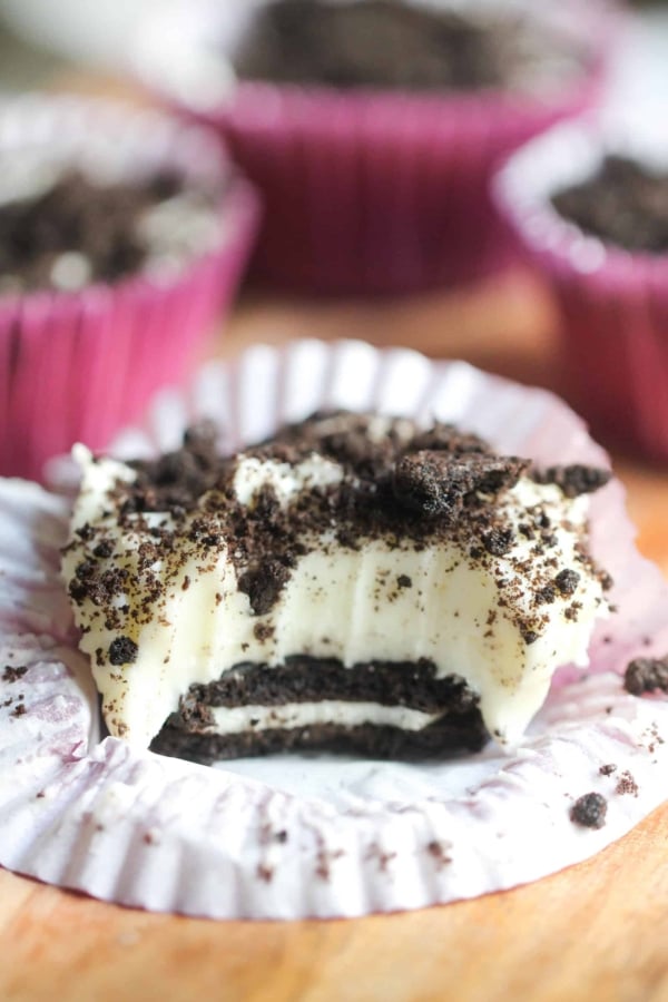 No Bake Mini Oreo Cheesecake on a counter with this muffin liner turned down and a bite missing so you can see the inside of the cheesecake.
