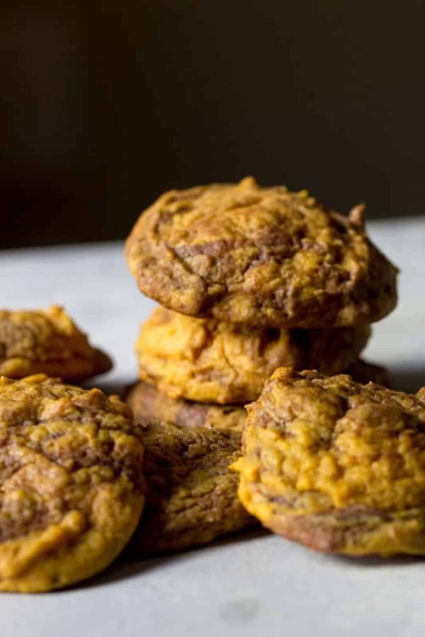 Close-up of a pile of homemade cookies with a golden-brown color, resting on a gray surface.