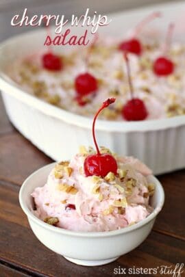 A small bowl of pink dessert topped with a cherry and nuts in front of a larger, matching dish with the same dessert.