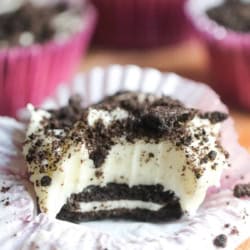 No Bake Mini Oreo Cheesecake on a counter with this muffin liner turned down and a bite missing so you can see the inside of the cheesecake.
