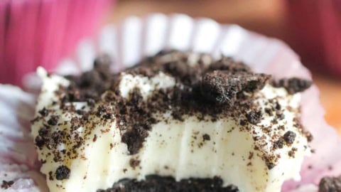 No Bake Mini Oreo Cheesecake on a counter with this muffin liner turned down and a bite missing so you can see the inside of the cheesecake.