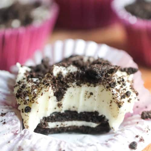 No Bake Mini Oreo Cheesecake on a counter with this muffin liner turned down and a bite missing so you can see the inside of the cheesecake.