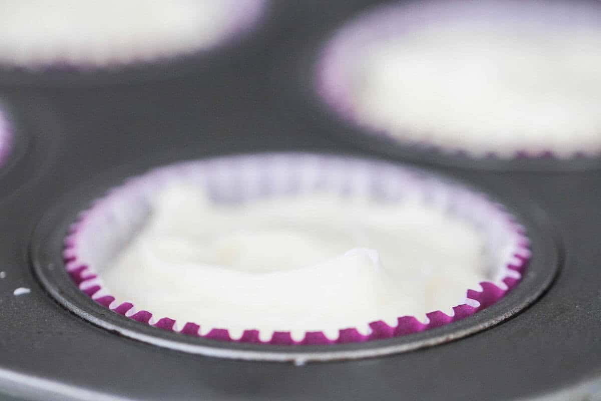 Close-up of a muffin tray filled with purple muffin liners and white batter.