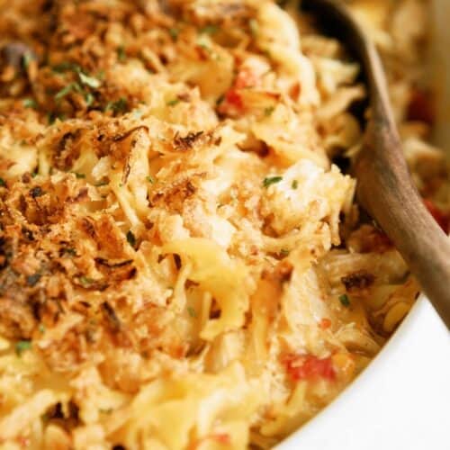 Close-up of a baked pasta casserole with a browned breadcrumb topping, being served with a wooden spoon.