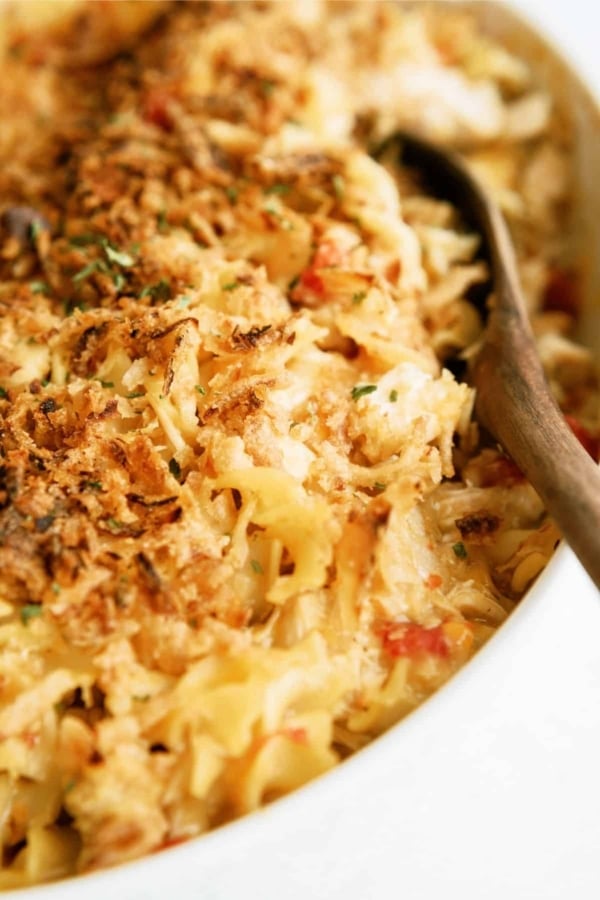 Close-up of a baked pasta casserole with a browned breadcrumb topping, being served with a wooden spoon.