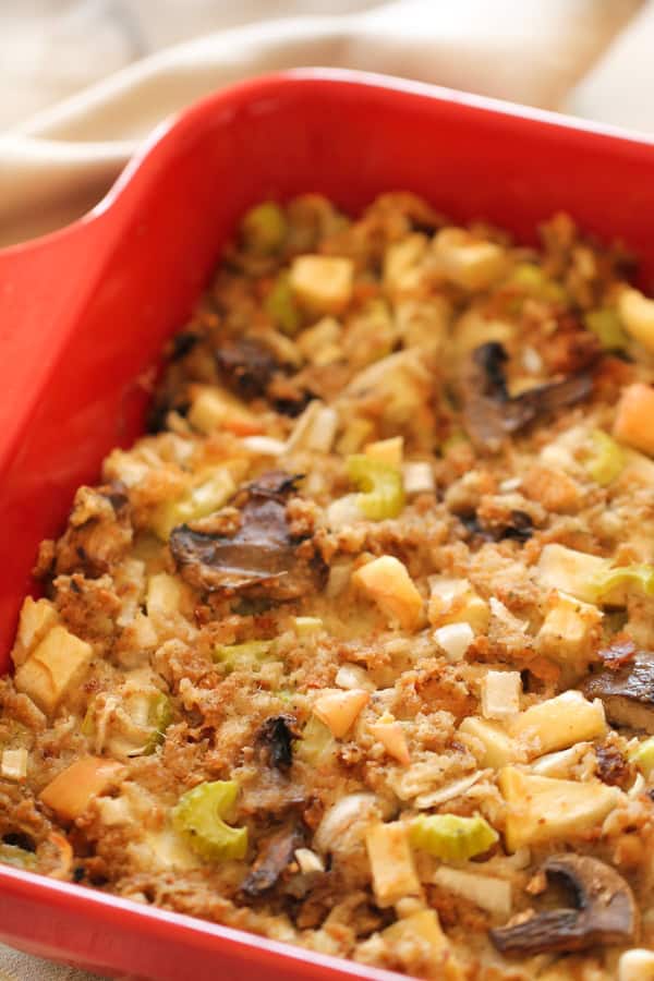 A red baking dish containing a homemade stuffing with visible chunks of bread, mushrooms, celery, and onions.