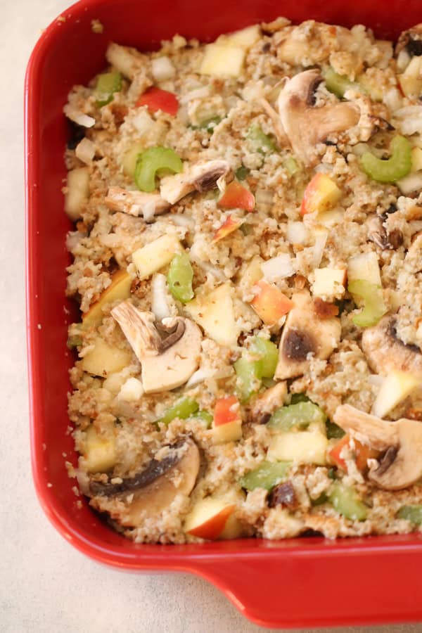 A baked dish in a red casserole dish, containing a mixture of vegetables including mushrooms, celery, onions, and pieces of apple.