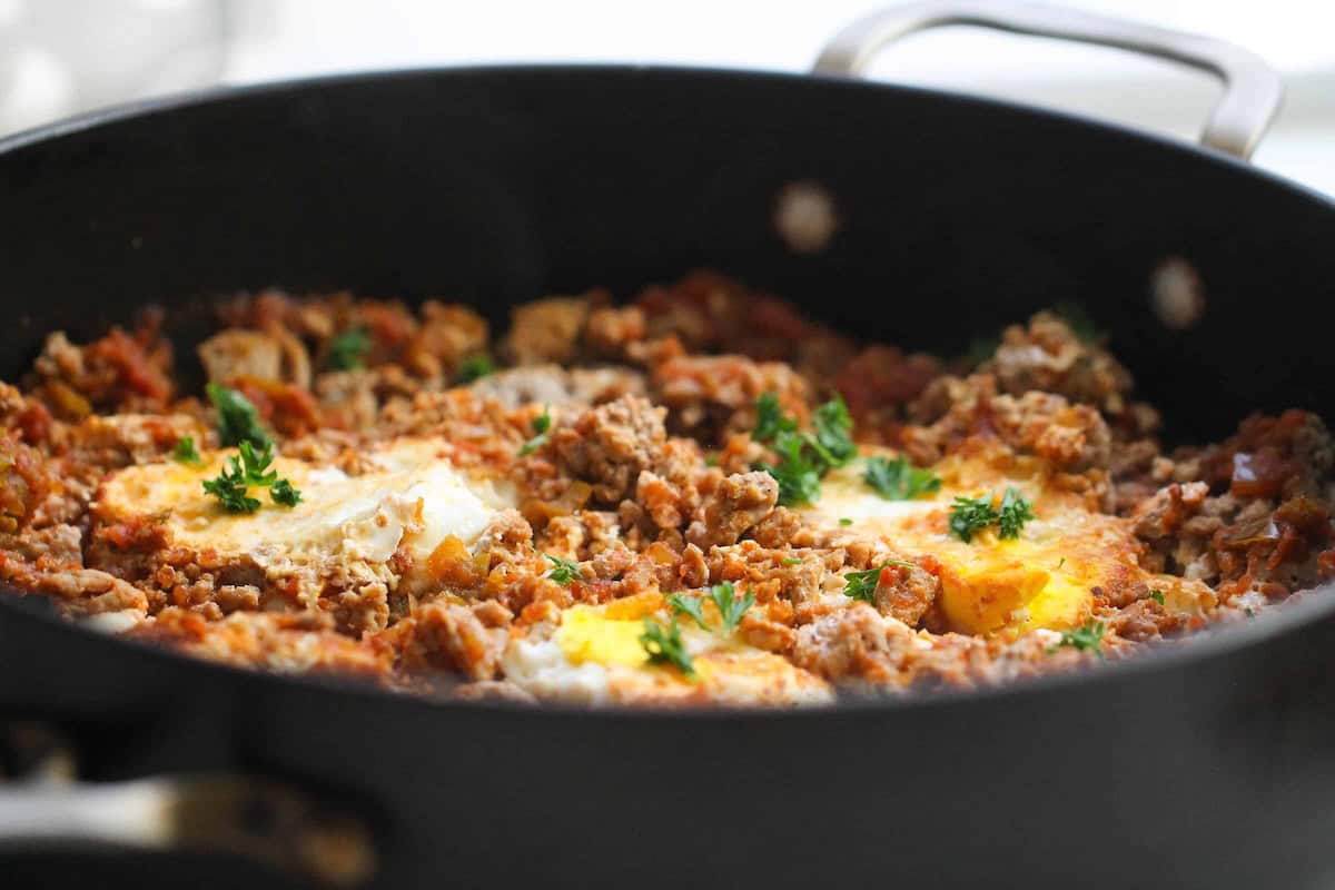 A pan with cooked ground meat, tomatoes, herbs, and poached eggs.
