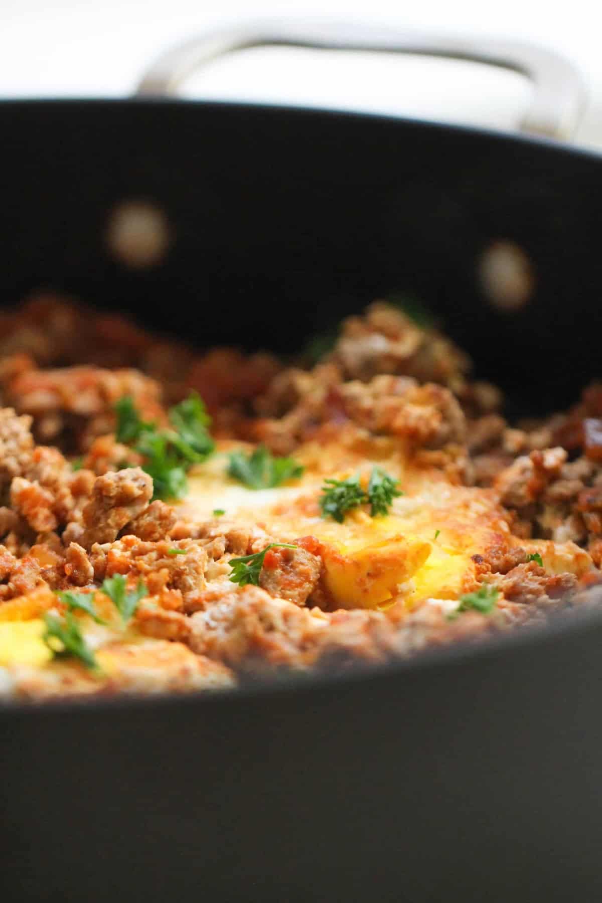 A skillet containing cooked ground meat topped with melted cheese and garnished with fresh parsley.