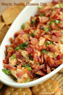 A serving dish filled with warm bacon cheese dip, garnished with chopped green onions. Crackers are partially visible around the dish.