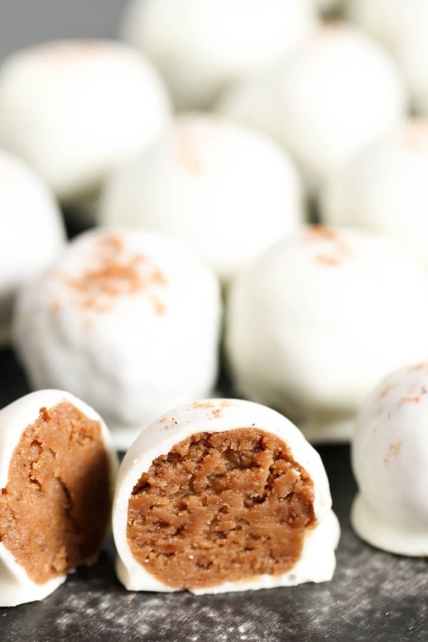 Close-up of white chocolate truffles, with the one in the foreground showing a bite taken out, revealing a peanut butter filling.