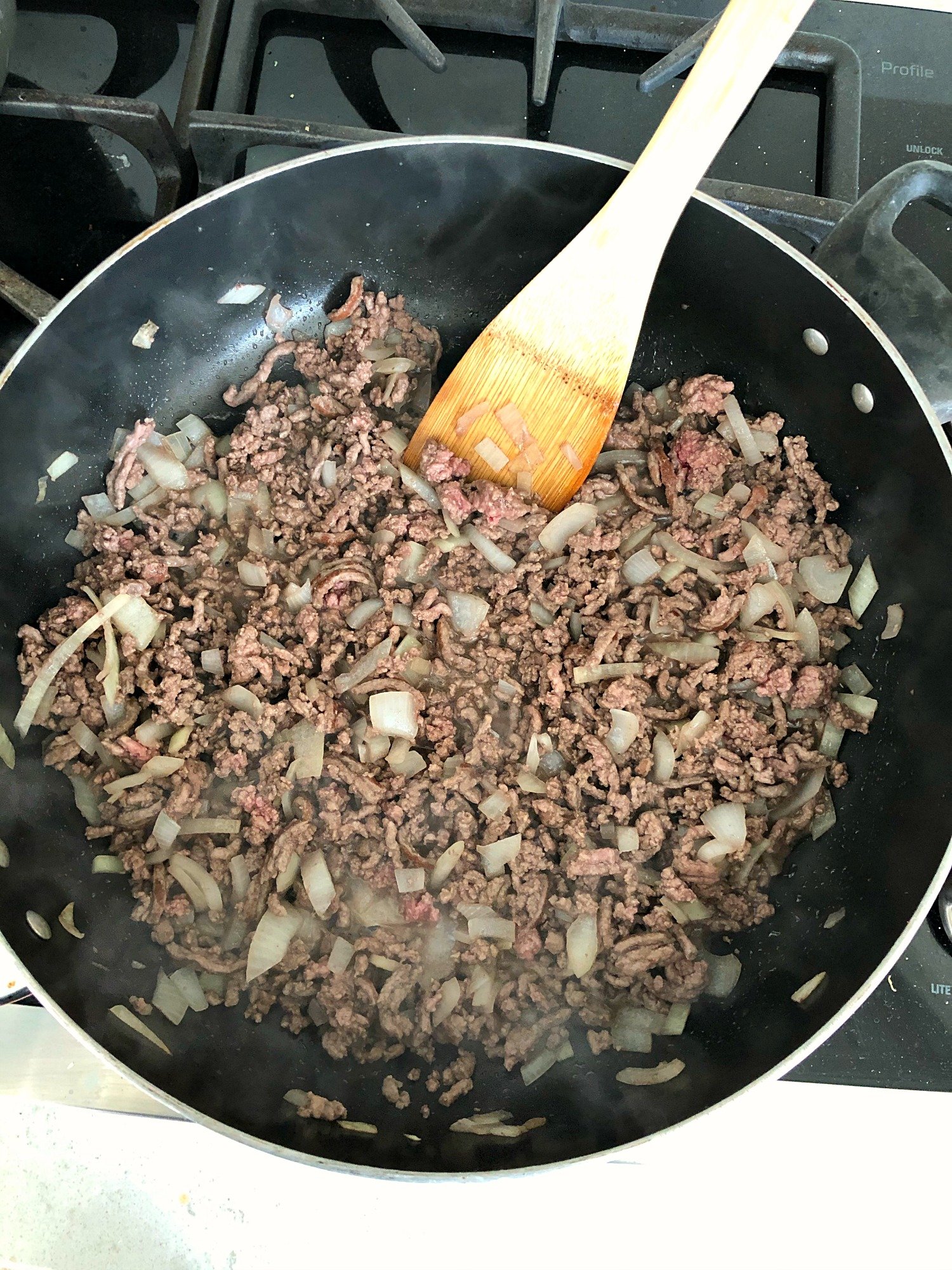 ground beef with onions being cooked in a skillet with wooden spoon