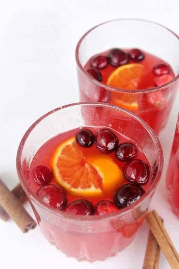 Two glasses filled with a red drink, each garnished with an orange slice and cranberries.