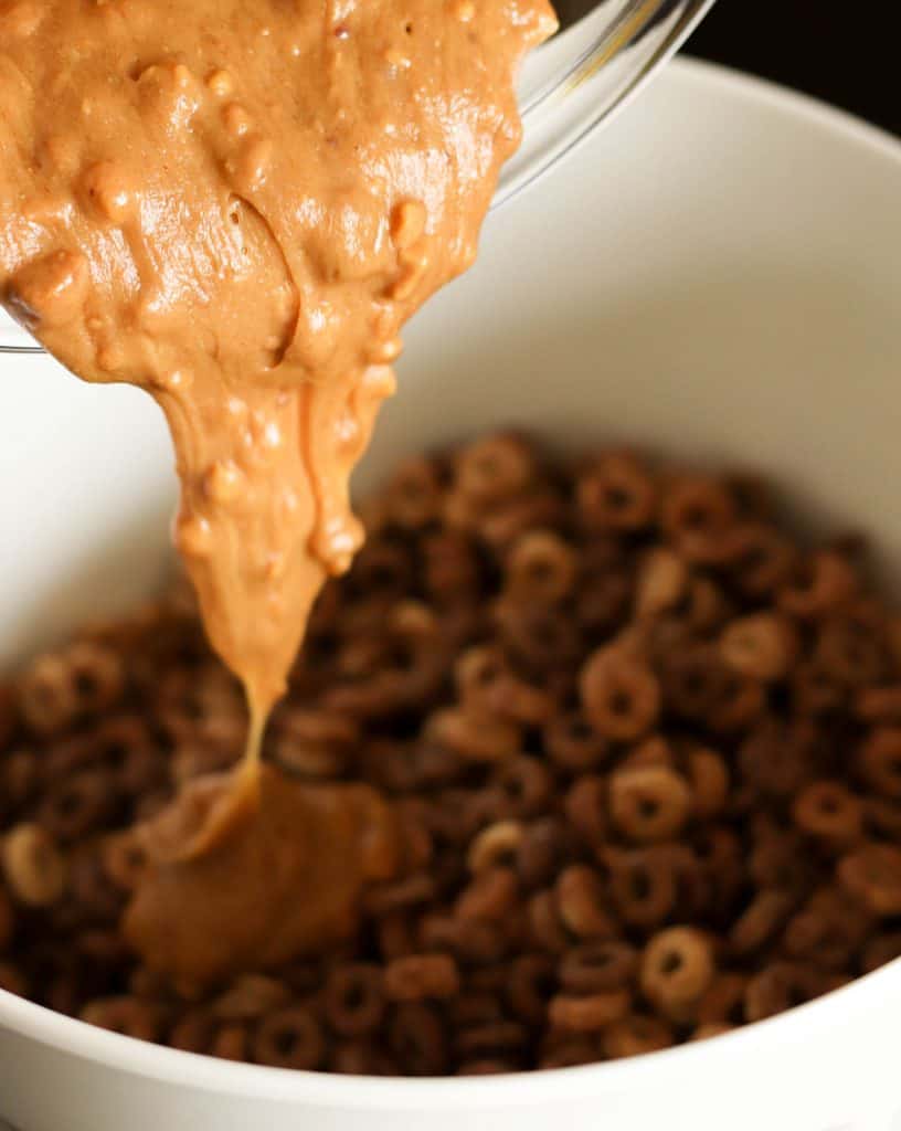 Adding peanut butter mixture to a bowl of cheerios.