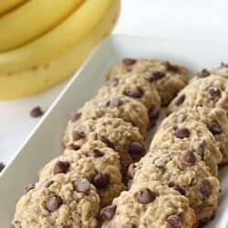 Soft banana oatmeal cookies on a white serving plate. With Bananas in the background.