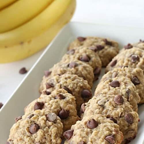 Soft banana oatmeal cookies on a white serving plate. With Bananas in the background.