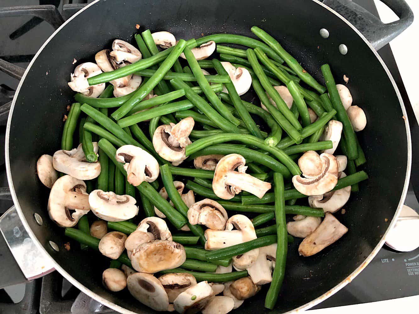 Green beans and mushrooms in a large stir fry pan