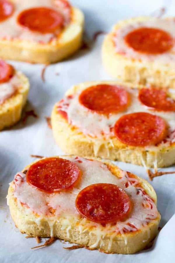 Slices of bread topped with melted cheese, tomato sauce, and pepperoni, arranged on a parchment-lined surface.