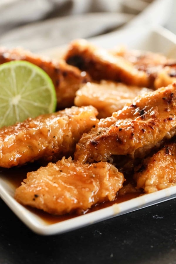 Baked Honey Chicken Tenders on a white serving plate with a fresh lime halved.