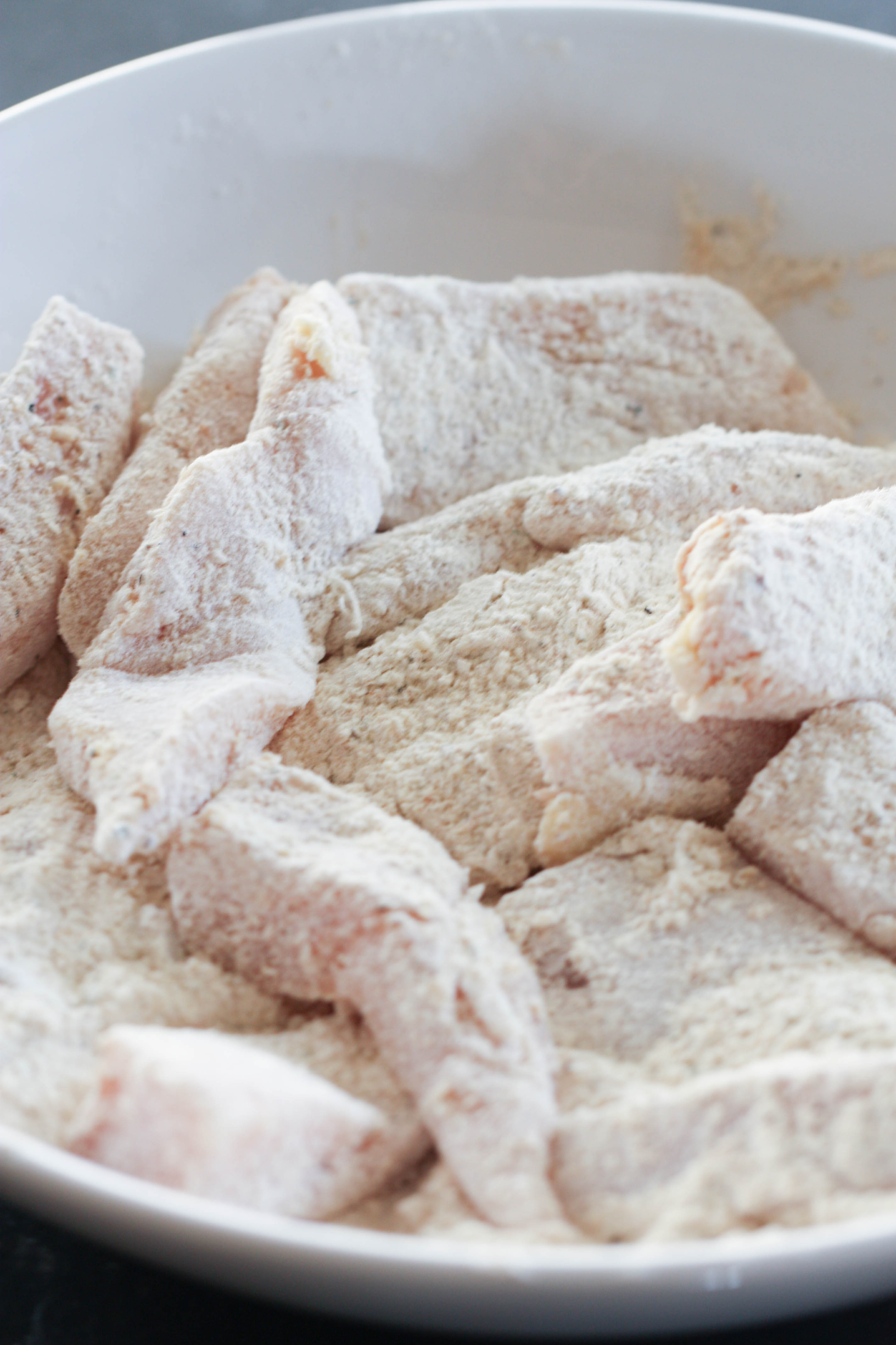 chicken tenders dredged in flour in a white bowl