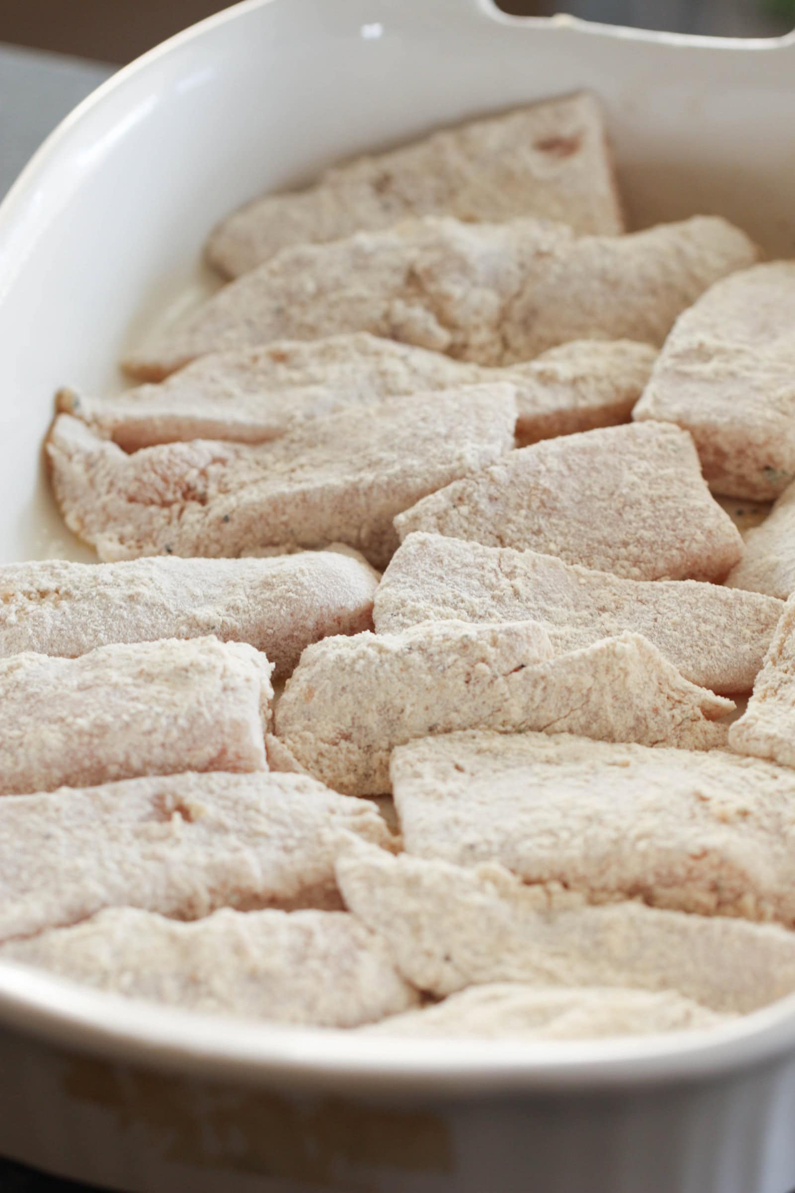 chicken tenders dredged in flour in a white bowl